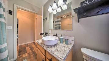 A bathroom with a white sink, a mirror, and a toilet. There is a towel rack and a shelf above the mirror.
