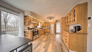 A modern kitchen with wooden cabinets, a stainless steel refrigerator, and a large window overlooking a balcony. - Meadville Home: Private Yard & Fishing Nearby (Meadville)