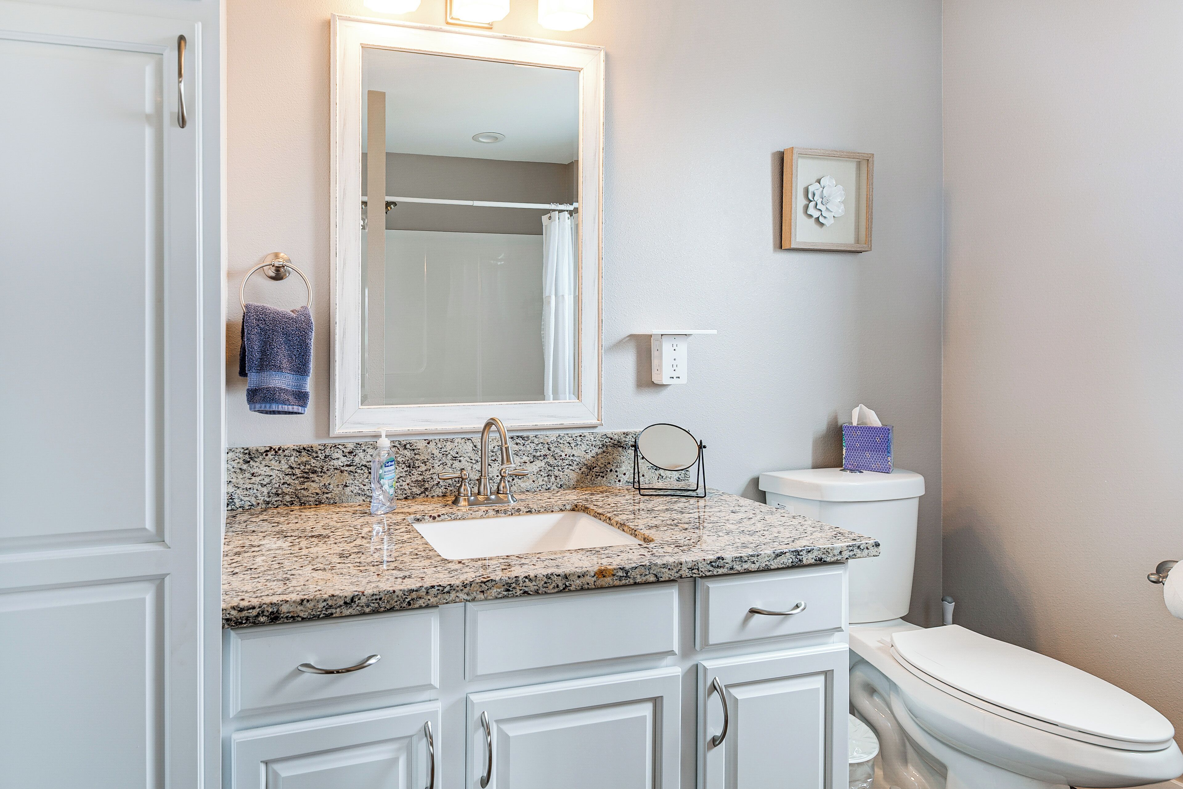 A bathroom with a granite countertop sink, white cabinets, a white toilet, and a mirror above the sink.