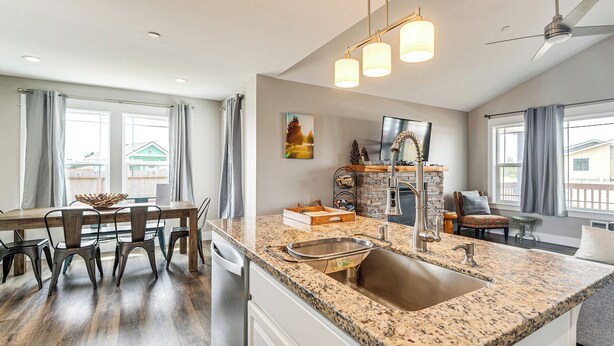 A modern kitchen with a granite countertop, stainless steel sink, and a dining area with a wooden table and chairs. - Modern Ocean Shores Home, 2 Mi to Beach! (Ocean Shores)