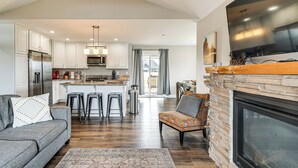 A spacious living room with a fireplace, a kitchen with white cabinets, and a dining area with a large TV. - Modern Ocean Shores Home, 2 Mi to Beach! (Ocean Shores)
