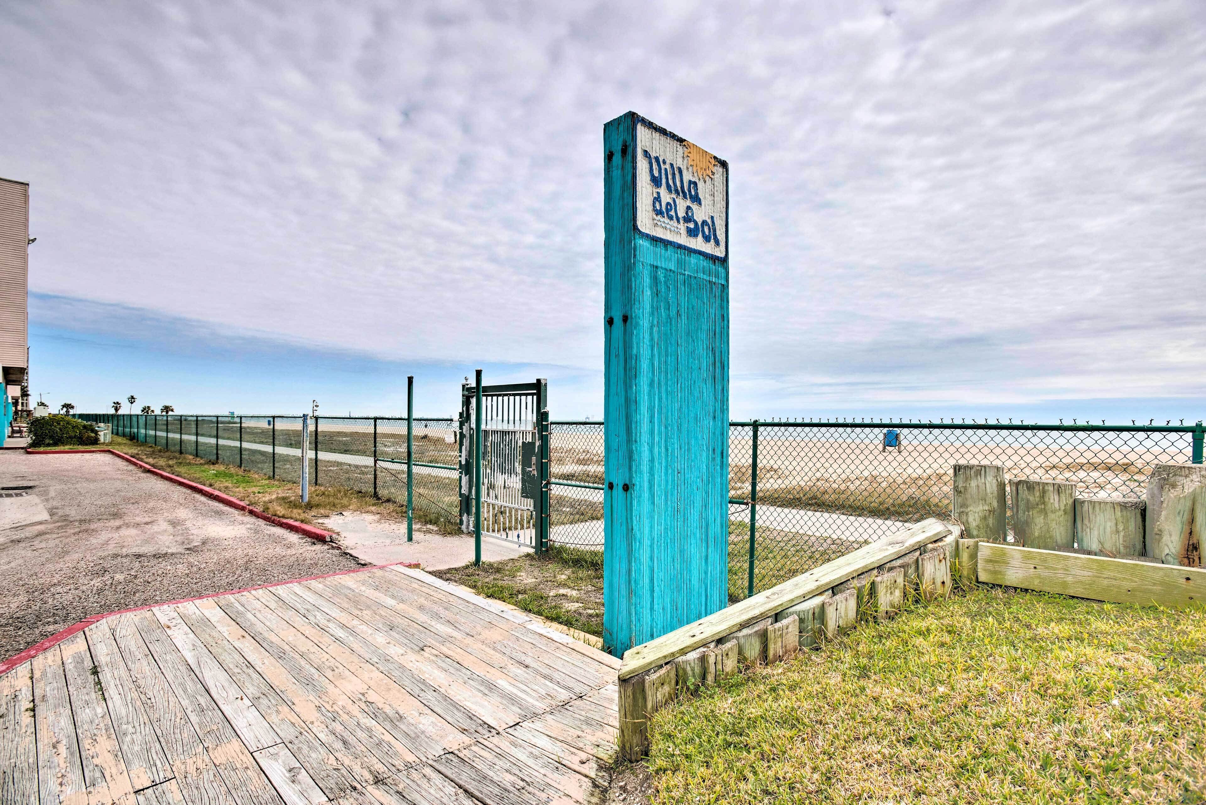Une promenade en bois mène à une zone de plage où un panneau indique « Villa del Sol ».