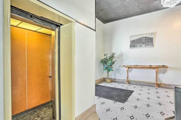 An interior hallway with a wooden door, a potted plant, a small table, and a patterned floor.