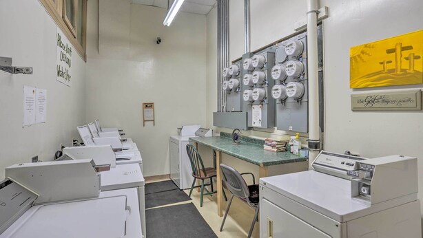 A laundry room with multiple washing machines, a desk, and a chair.