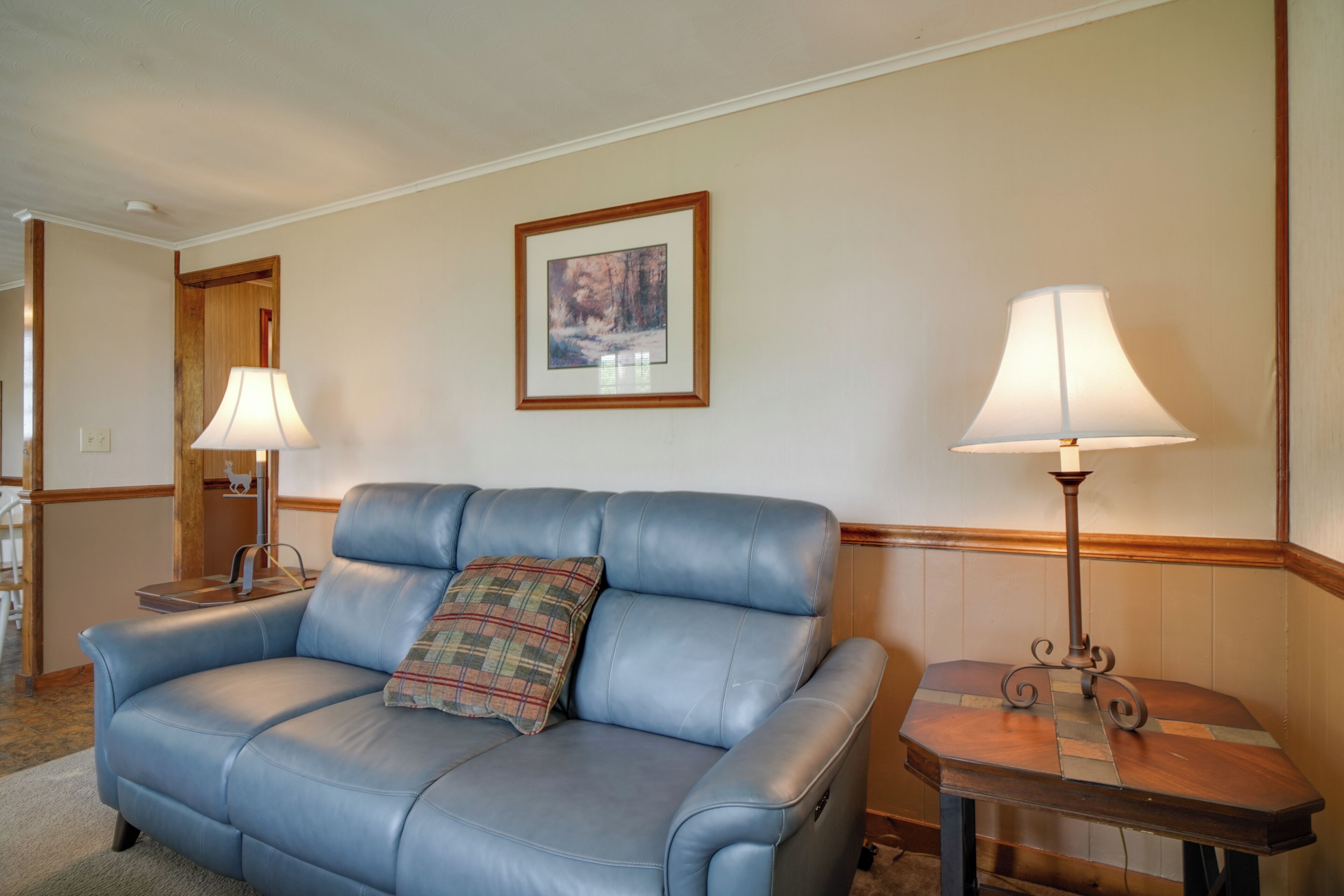 Ein blaues Ledersofa mit einem karierten Kissen, zwei Tischlampen und einem gerahmten Bild an der Wand.