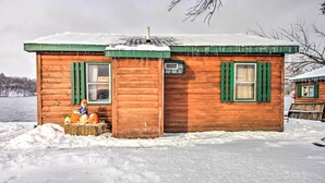 Una cabaña de madera con contraventanas verdes, un ventanal pequeño y un techo cubierto de nieve.