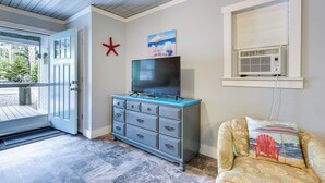 Una habitación con una puerta, un aparador azul, un televisor, un cojín con motivos playeros y una decoración de estrella de mar.