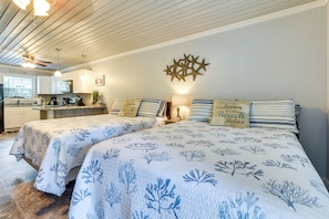 Een slaapkamer met twee bedden, een plafondventilator, een keuken op de achtergrond en decoratieve kussens.