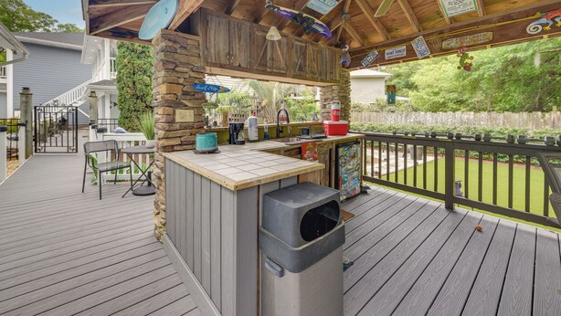 Una terraza de madera con una estación de barbacoa, mobiliario exterior y vistas al jardín trasero.