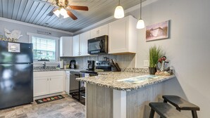 Una cocina con una isla central, armarios blancos, microondas, cafetera y ventilador de techo.