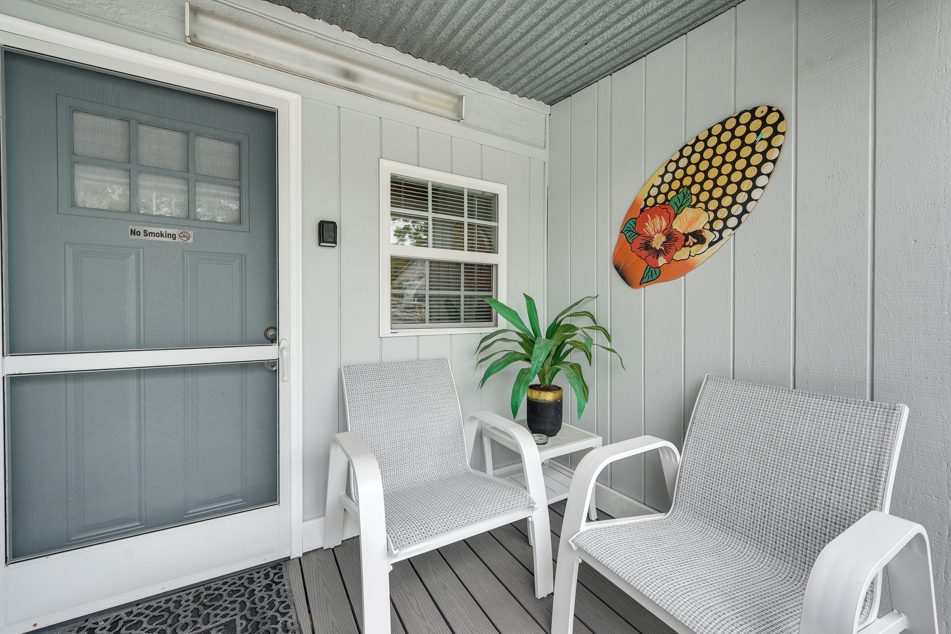 A porch with two white chairs, a potted plant, and a 'No Smoking' sign on a door.