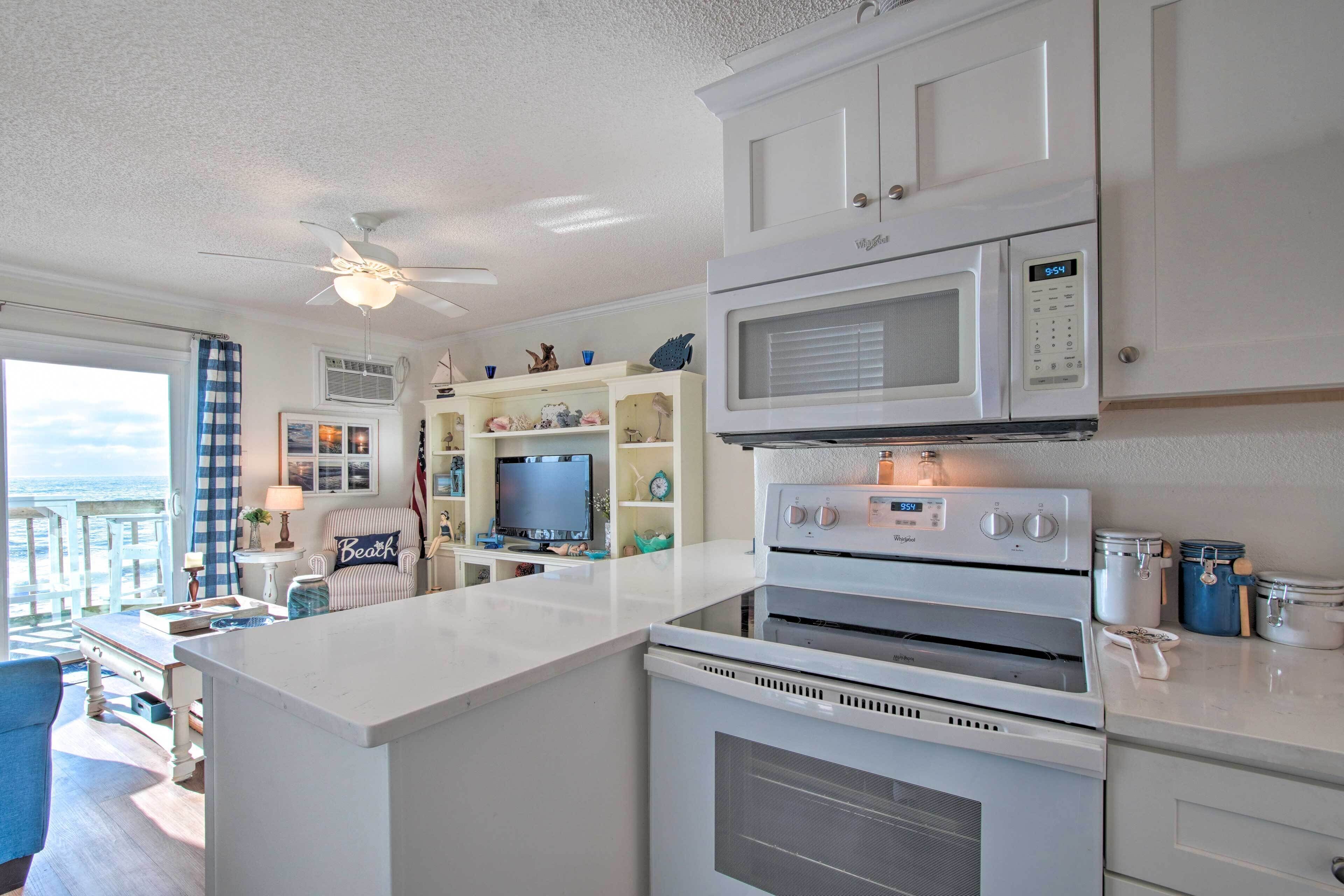 A kitchen with white cabinets, a microwave, an oven, and a television on a stand.