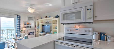 A kitchen with white cabinets, a microwave, an oven, and a television on a stand.