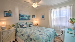 A bedroom with a bed, a ceiling fan, a dresser, a window with curtains, and wall art. - Oceanfront Condo w/ Views in North Topsail Beach! (Sneads Ferry)