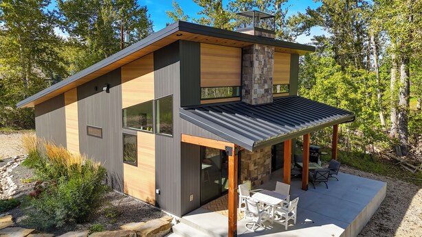 A modern two-story house with a patio, large windows, and a stone fireplace. - Rock Creek Retreat: Creekside Cabin Near Red Lodge (Red Lodge)