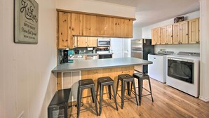 Una cocina con armarios de madera, un microondas integrado, una isla grande con taburetes y una lavadora.