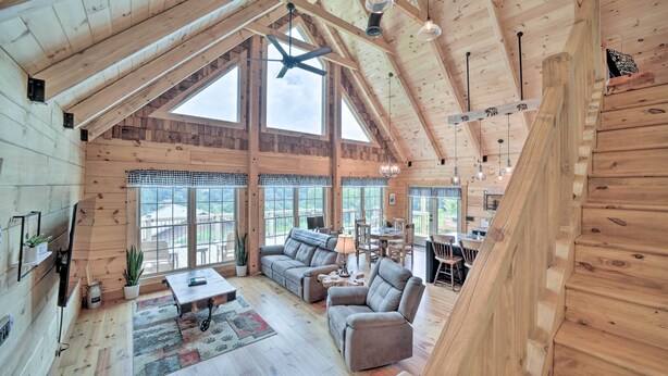 A spacious loft-style room with a high ceiling, large windows, and a cozy seating area with a sofa and chairs. - Luxe Log Cabin w/ Modern Finishes & Mtn Views (Maggie Valley)