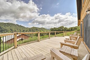 A wooden deck with outdoor seating and a view of a forested hill. - Luxe Log Cabin w/ Modern Finishes & Mtn Views (Maggie Valley)