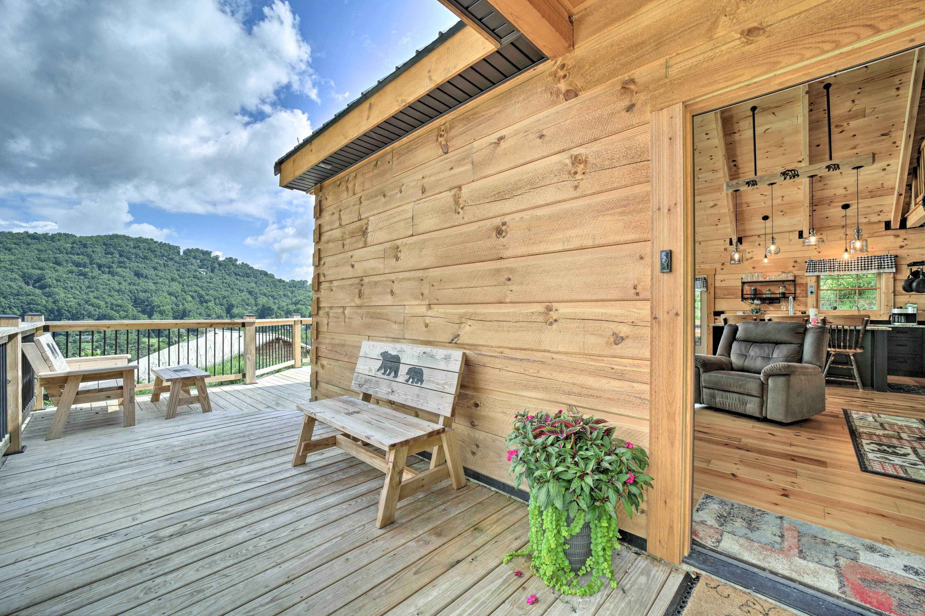 Una terraza de madera con mobiliario exterior, una planta en maceta y vistas a una colina boscosa.