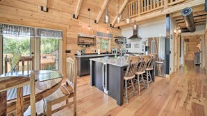 A spacious kitchen with wooden cabinetry, a central island, and a dining area with wooden chairs. - Luxe Log Cabin w/ Modern Finishes & Mtn Views (Maggie Valley)