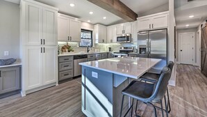 A modern kitchen with white cabinets, stainless steel appliances, and a central island with bar stools. - Hike, Bike & Unwind: Bella Vista Family Home! (Bella Vista)
