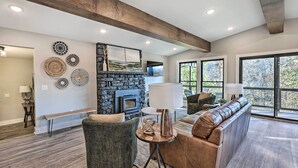 A modern living room with a stone fireplace, a large window, and a cozy seating area. - Hike, Bike & Unwind: Bella Vista Family Home! (Bella Vista)