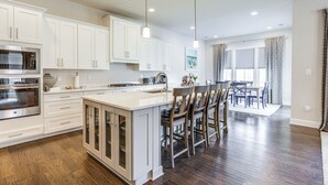 A spacious kitchen with white cabinetry, a large island with bar stools, a built-in oven, and pendant lighting. - Near Bethany Beach: Resort-style Home w/ Views (Ocean View)