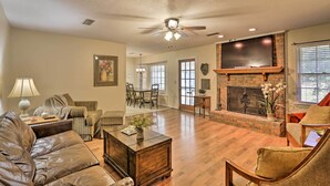 A spacious living room with a fireplace, leather sofa, and a dining area in the background. - Quiet Dothan House With Fenced Yard + Fire Pit! (Dothan)