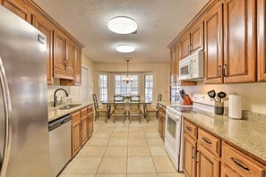 A kitchen with wooden cabinets, stainless steel appliances, a dining table with chairs, and a window with a view. - Quiet Dothan House With Fenced Yard + Fire Pit! (Dothan)