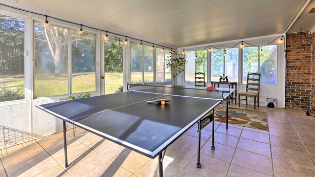 A ping pong table in a sunlit room with large windows, a brick wall, and a tiled floor. - Quiet Dothan House With Fenced Yard + Fire Pit! (Dothan)