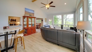 A spacious living area with a large gray sectional sofa, wooden dining table, and chairs, a kitchen area with modern appliances, and large windows offering a view of the outdoors. - Remote Smoky Mtn Escape w/ Views & Trail Access! (Franklin)