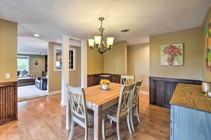 A dining area with a wooden table, white chairs, and a chandelier. - Peaceful Ranch-style Camano Home on 5 Acres! (Camano Island)