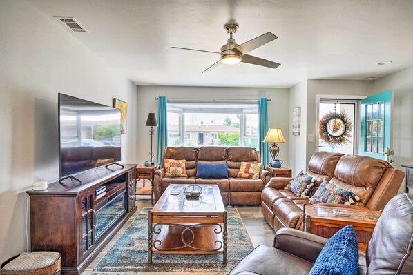 A living room with a brown leather sofa, a coffee table, a TV, and a ceiling fan.