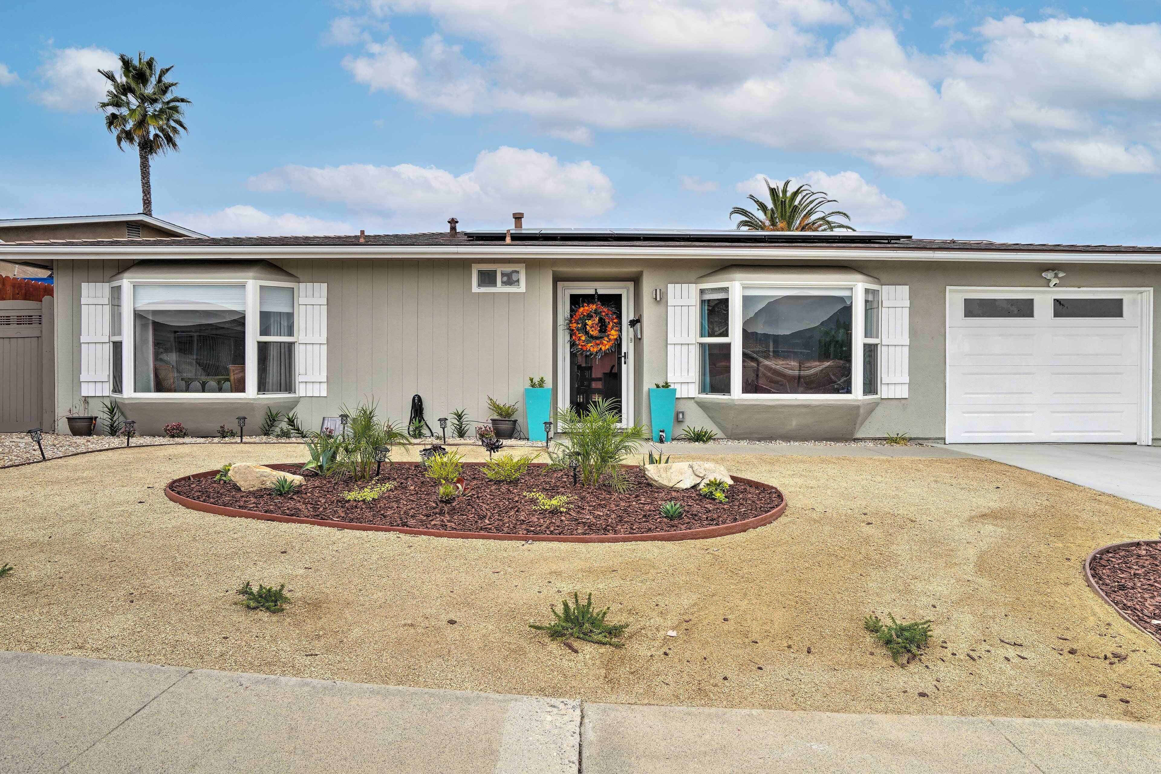 A single-story house with a front porch, a garage, and a landscaped front yard with plants and mulch.