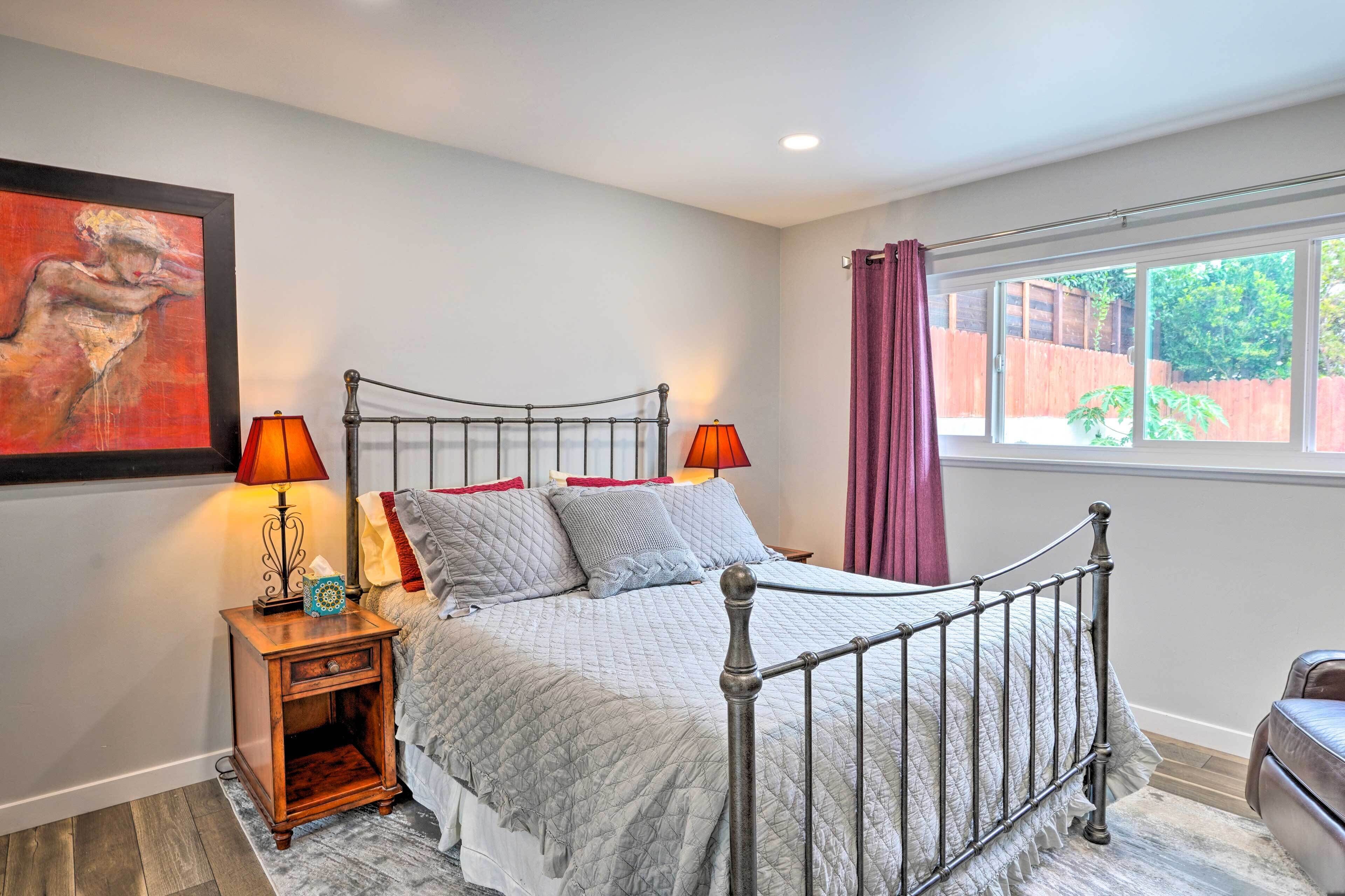 A bedroom with a bed, nightstand, and window with curtains.