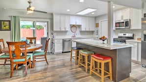 A modern kitchen with white cabinets, a central island with stools, a dining table with chairs, and a ceiling fan. - San Marcos Home w/ Patio & Grill - Walk to Lake! (San Marcos)