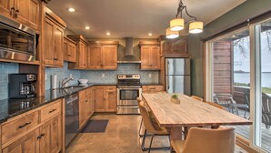 A modern kitchen with wooden cabinets, stainless steel appliances, and a large dining table with chairs. - Pelican Lake Retreat w/ Fire Pit, Dock & Grill! (Pequot Lakes)