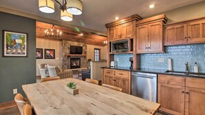 A kitchen with wooden cabinets, a stone fireplace, and a dining area with a large wooden table. - Pelican Lake Retreat w/ Fire Pit, Dock & Grill! (Pequot Lakes)