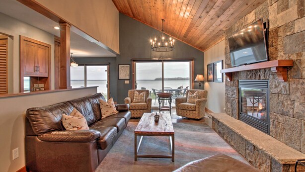 A spacious living room with a stone fireplace, leather sofas, and a large window overlooking a body of water. - Pelican Lake Retreat w/ Fire Pit, Dock & Grill! (Pequot Lakes)
