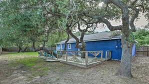 A blue house with a wooden deck and a tree in the yard.