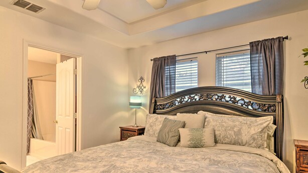 A bedroom with a large bed, a nightstand, a lamp, a window with curtains, and a door leading to a bathroom.