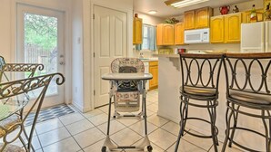A kitchen with wooden cabinets, a microwave, and a refrigerator. There is a high chair and two bar stools.