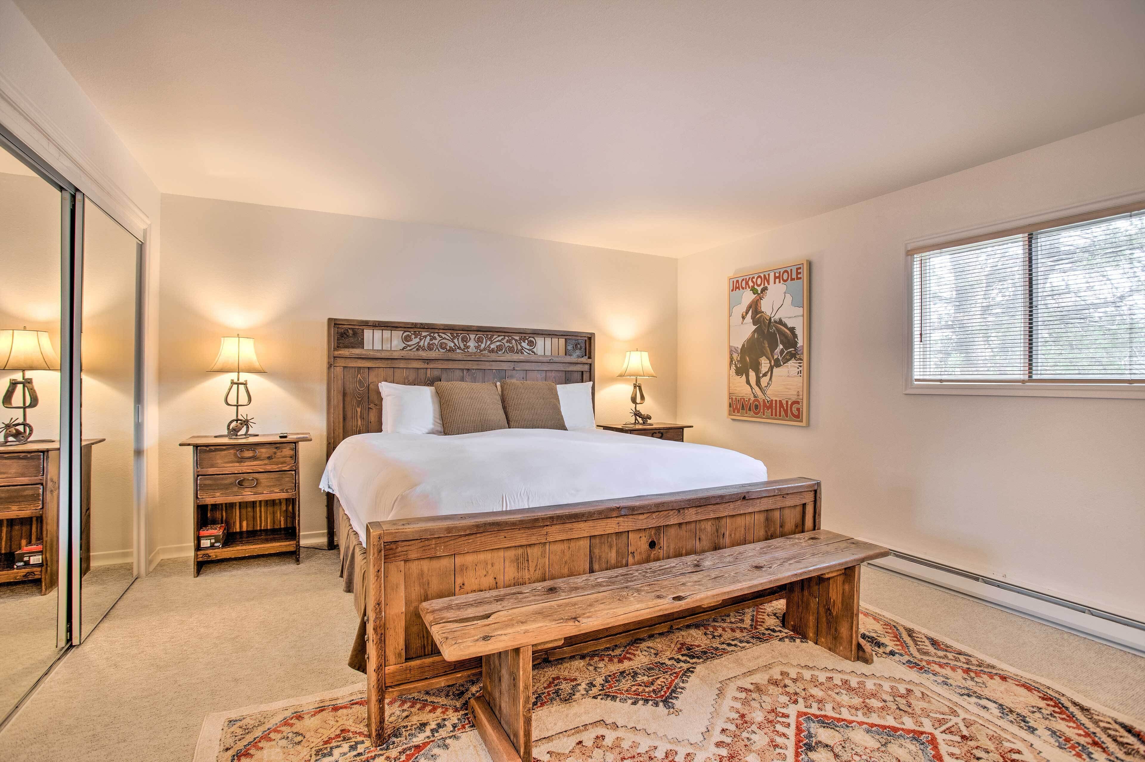 Une chambre avec un lit en bois, deux tables de chevet avec des lampes, un banc, un tapis et une affiche accrochée au mur.