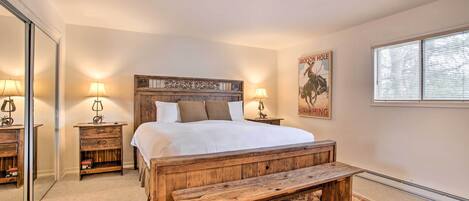 Une chambre avec un lit en bois, deux tables de chevet avec des lampes, un banc, un tapis et une affiche accrochée au mur.