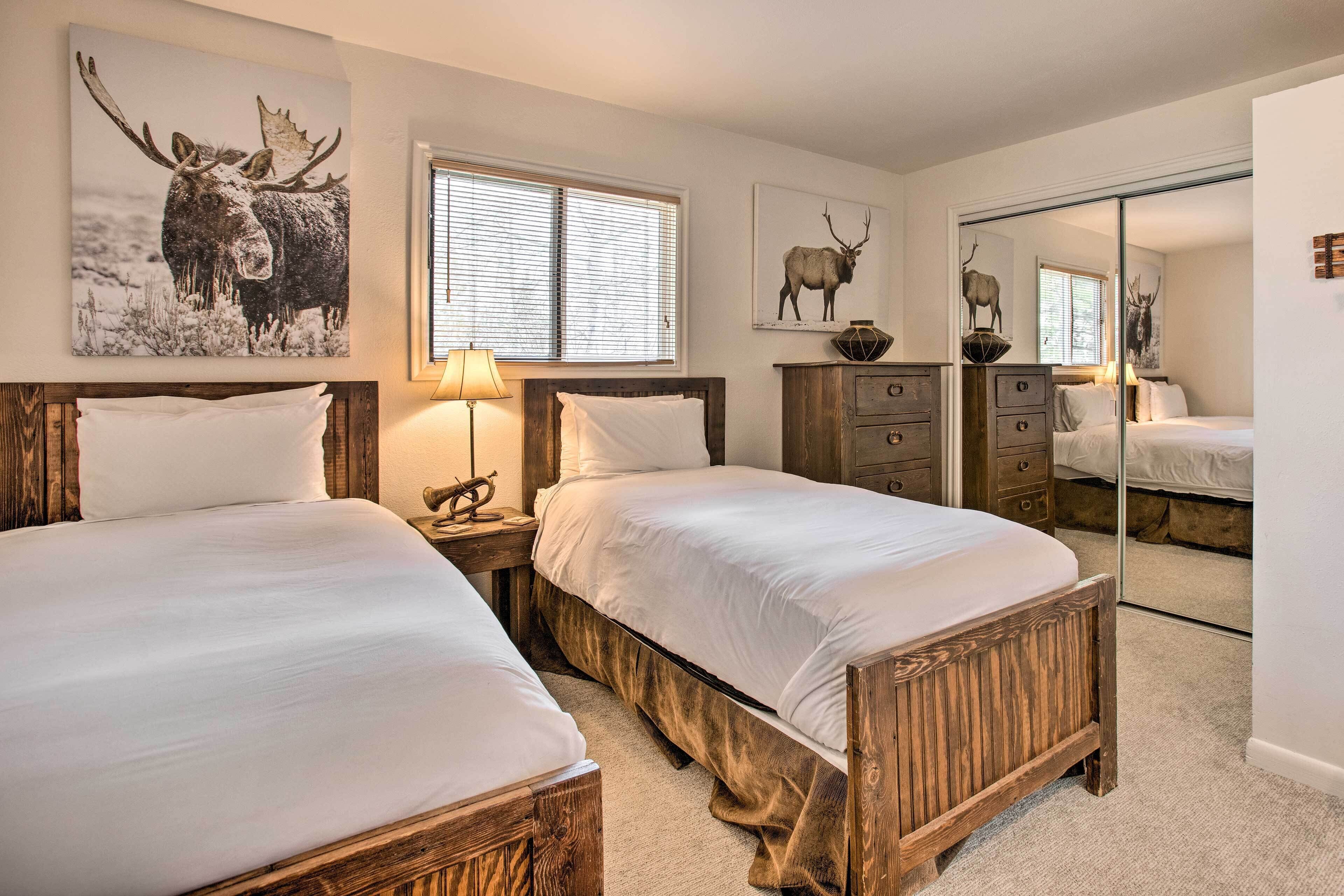A bedroom with two wooden beds, a window with blinds, and wall-mounted artwork of moose.
