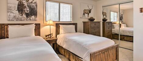 A bedroom with two wooden beds, a window with blinds, and wall-mounted artwork of moose.