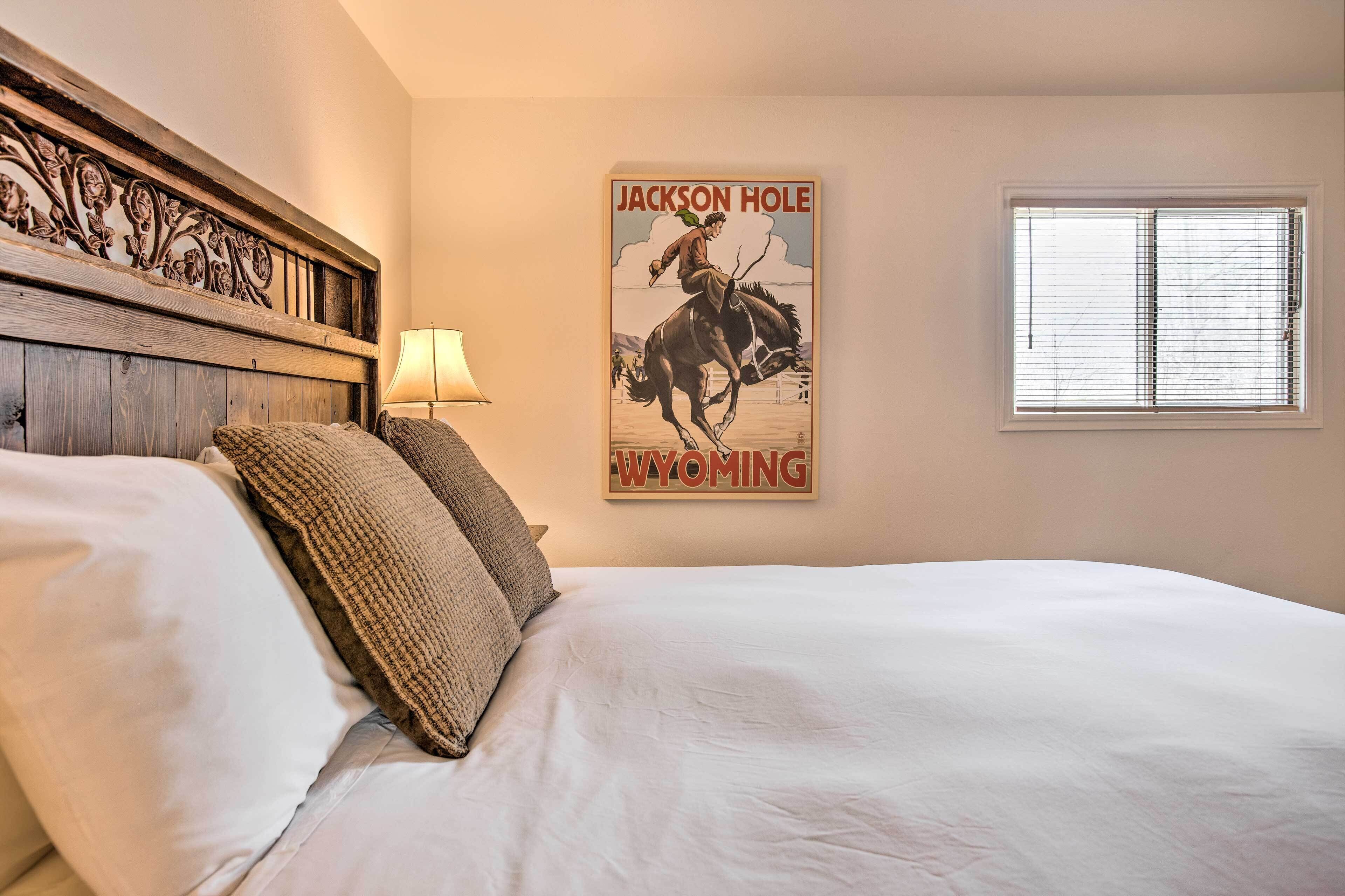 Une chambre à coucher avec un lit, des oreillers, une lampe, une affiche représentant un cow-boy à cheval et une fenêtre avec des stores.