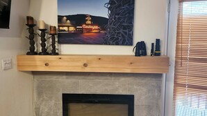 A fireplace with a stone surround, a wooden mantel with three candles, and a framed picture above it. - Skier's Dream: Upscale Condo By Teton Village! (Wilson)