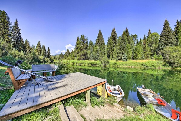 A wooden dock with a bench and fishing rods, a small boat, and a canoe by a calm lake surrounded by trees.