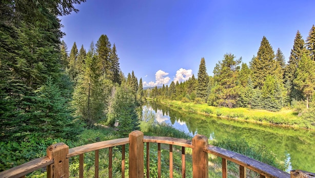 Una terraza de madera con vista a un río tranquilo, flanqueado por un bosque denso.